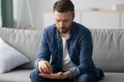 man in a denim shirt sitting on a couch looking at a tramadol pill on his palm
