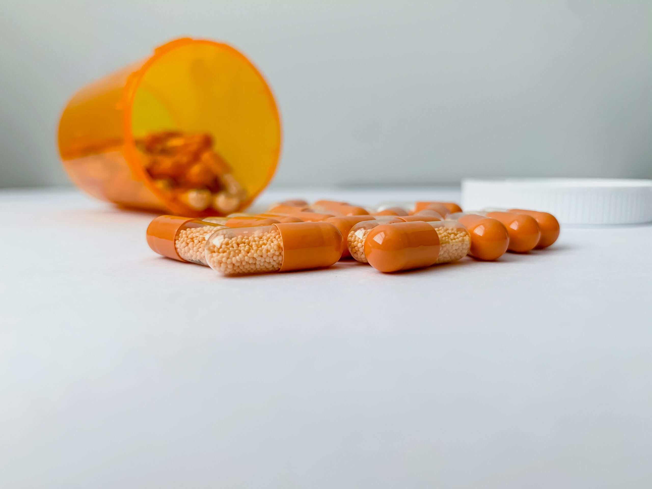An orange pill bottle with adderall capsules inside with half its contents spilled on a table