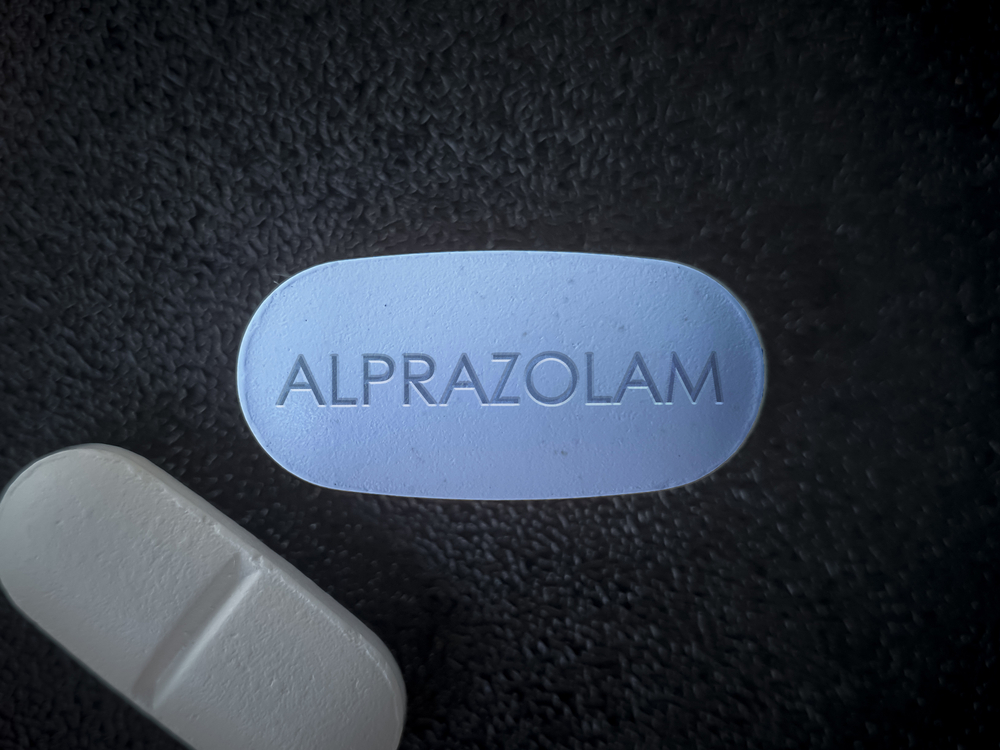 A blue alprazolam tablet on a black surface with a white pill on the side