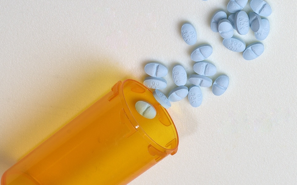 An orange bottle and scattered blue Xanax alprazolam pills on a white background