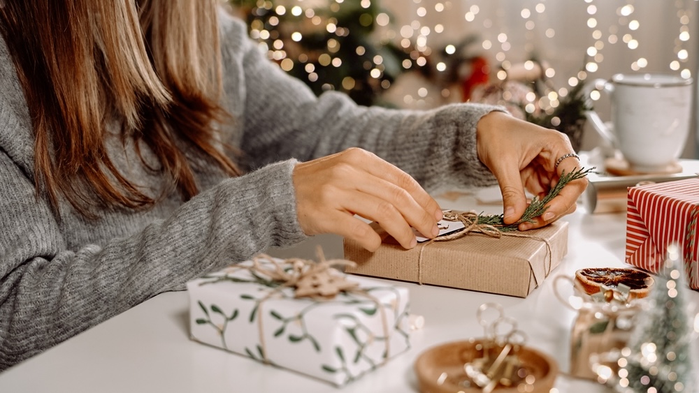 A woman in a gray sweater wrapping holiday gifts