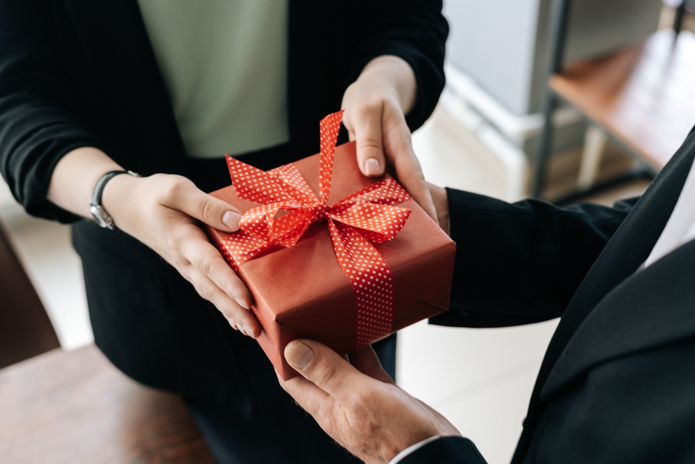 Closeup of two pairs of hands exchanging a holiday gift in a red box