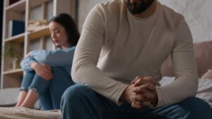 A couple sitting on the bed with the man’s black turned away from his female partner hugging her knees