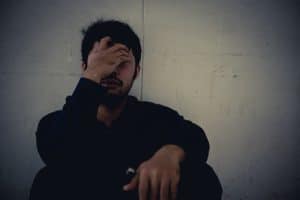 Man addicted to meth and crack sitting on the floor covering his face
