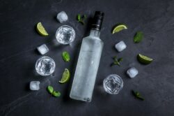 A vodka bottle surrounded by glasses and limes.