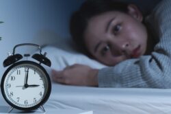 Woman lies awake in bed looking at the bedside clock