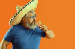 An old man with a Mexican hat drinking a shot of tequila