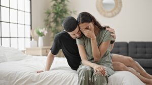Husband and wife sitting on the bed comforting each other as they deal with addiction