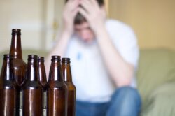 Man in a white shirt feeling depressed with several empty beer bottles