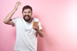 Man with white shirt holding a beer wondering if beer has 100% alcohol